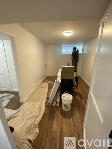 A man is painting a wall in a room with a bucket of paint on the floor.