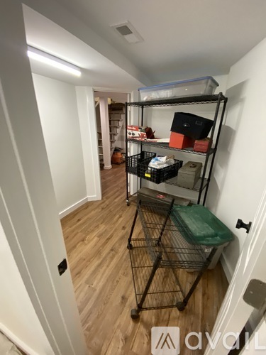A narrow hallway with a shelving unit and a green laundry basket.
