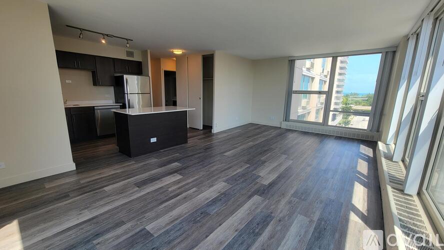 A spacious room with a kitchen area and a large window overlooking a cityscape.