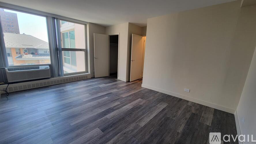 A room with wooden flooring and a large window overlooking a building.
