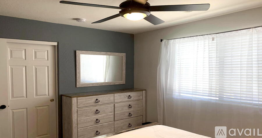 A bedroom with a bed, dresser, mirror, and window with blinds.