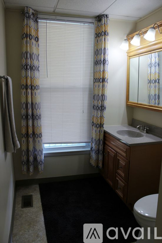 A bathroom with a sink, toilet, and a window with a curtain.