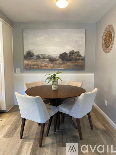 A dining room with a large painting on the wall and a wooden table with white chairs.