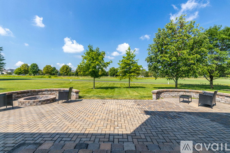 A circular brick patio with a fire pit and seating area in the middle of a grassy field.