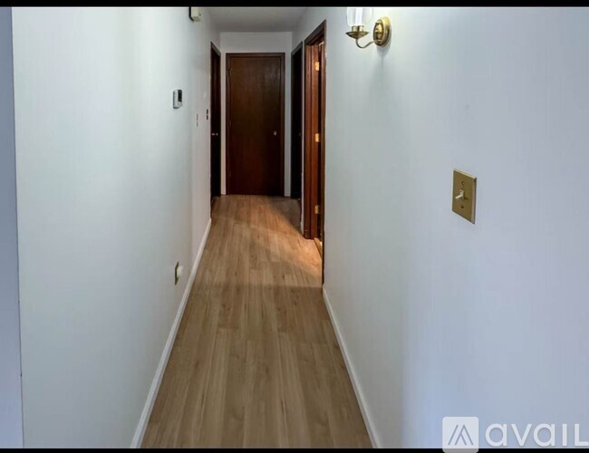 A long hallway with a wooden floor and a brown door at the end.