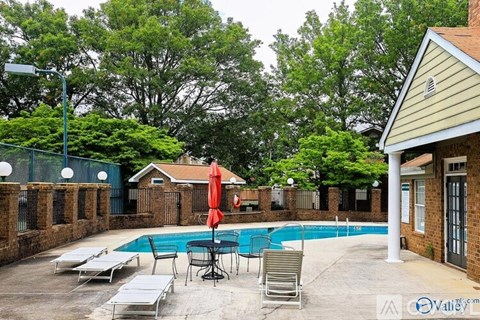 A pool area with a table and chairs and a red umbrella.