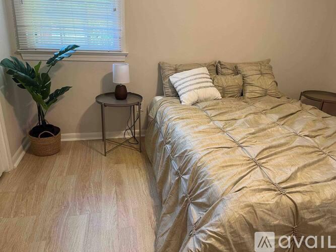 A bedroom with a bed, a plant, and a table with a lamp on it.