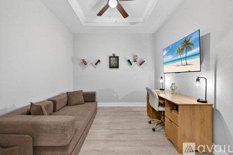 A living room with a brown couch, a desk with a chair, and a television displaying a beach scene.