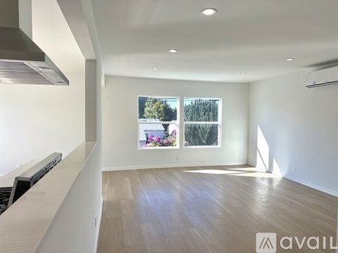 A spacious room with wooden flooring and a large window showing an outdoor view.