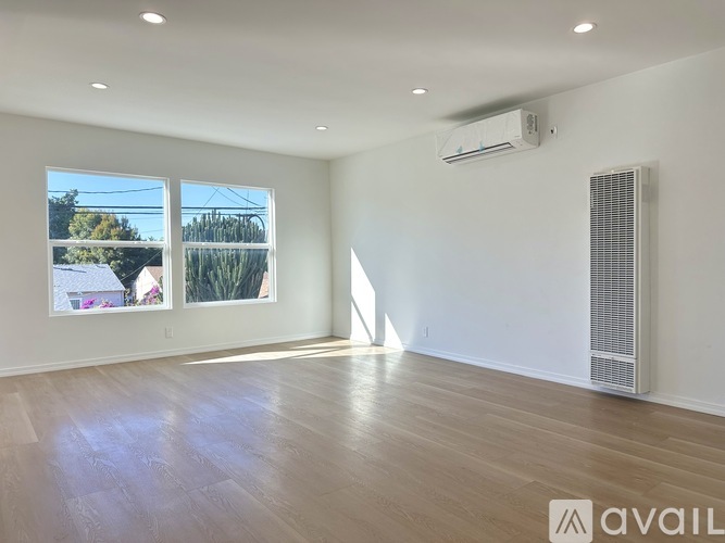 A spacious room with wooden flooring and a large window overlooking a residential area.