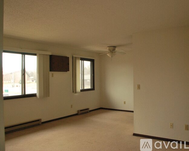 A spacious room with a ceiling fan and two windows.