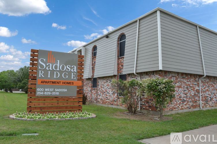 A sign for Sadosa Ridge Apartment Homes is in front of a brick building.