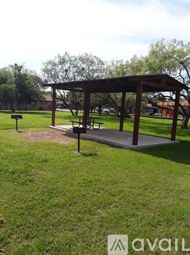 A wooden pavilion with a picnic table sits in a grassy field.
