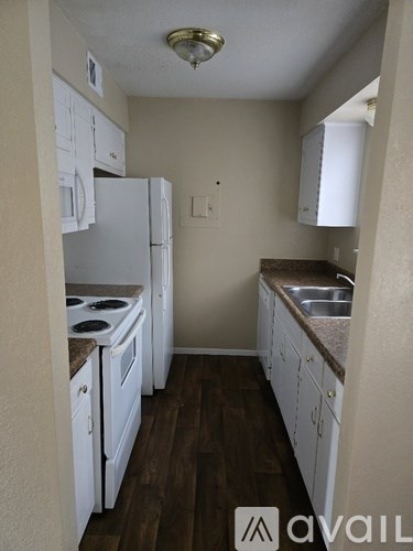 A kitchen with white appliances and brown wood floors.