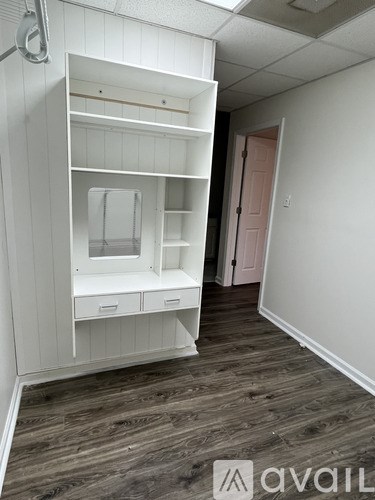 A white built-in closet with drawers and shelves in a room with wood flooring.