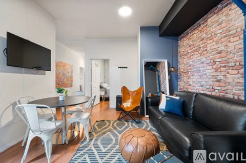A living room with a black leather couch and a glass table with white chairs.