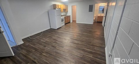 A room with wooden flooring and a kitchenette in the background.