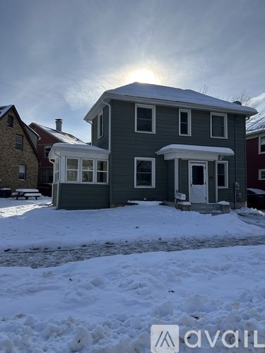 A house with a grey front and a red roof is surrounded by snow.