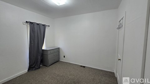 A small bedroom with a bed, dresser, and carpeted floor.