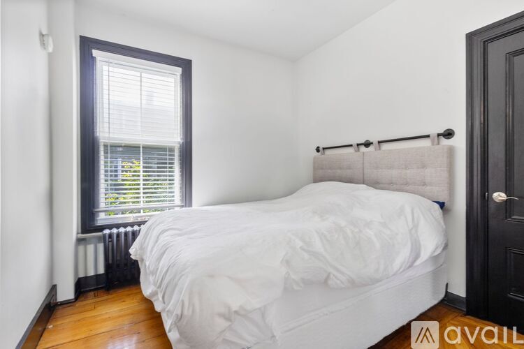 A bedroom with a white bed and a window with blinds.