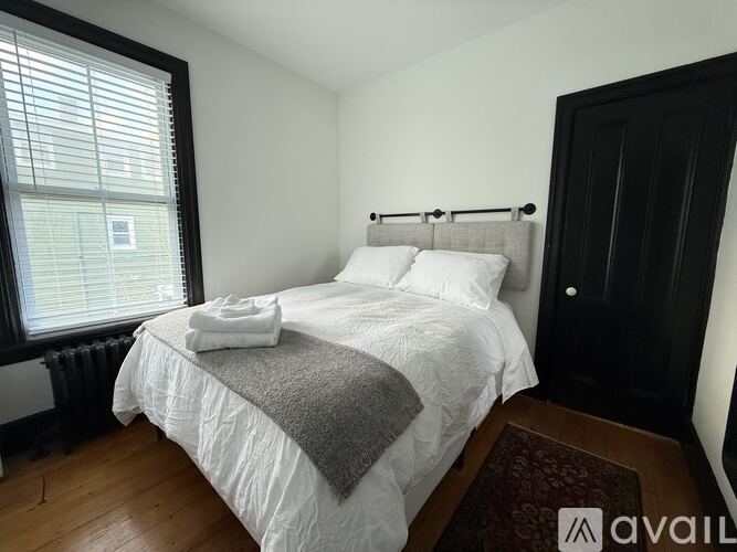 A bedroom with a white bed and a window with blinds.