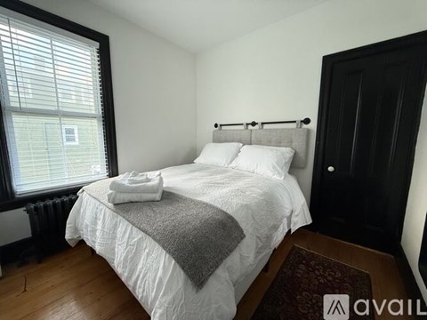A bedroom with a white bed and a window with blinds.