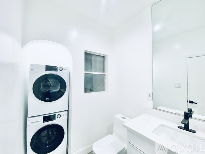 A white bathroom with a washing machine and a mirror.