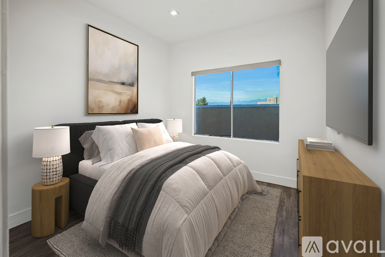 A bedroom with a large bed, a lamp, a painting, and a window overlooking a body of water.