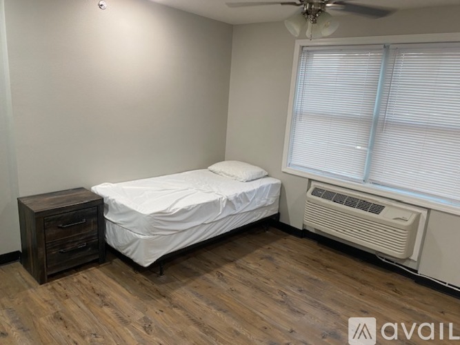 A bedroom with a bed, nightstand, and window with blinds.
