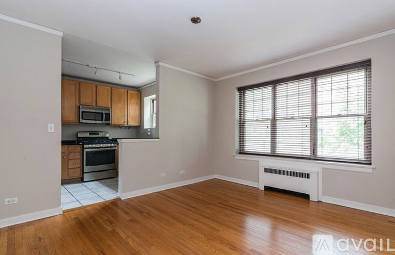 A spacious living room with wooden floors and a kitchen area in the background.