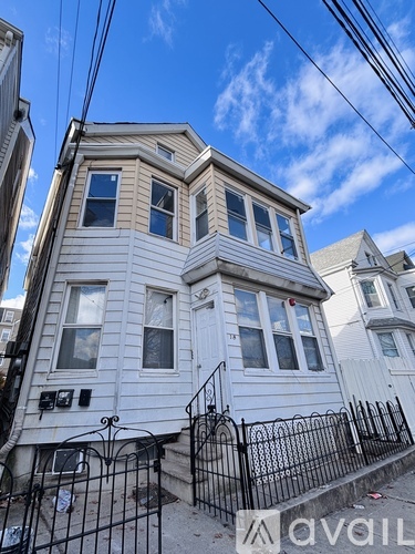 A white two-story house with a black iron fence in front.