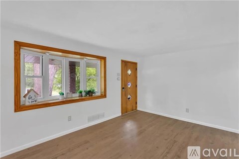 A room with a wooden door and a window with a view of trees and a house.