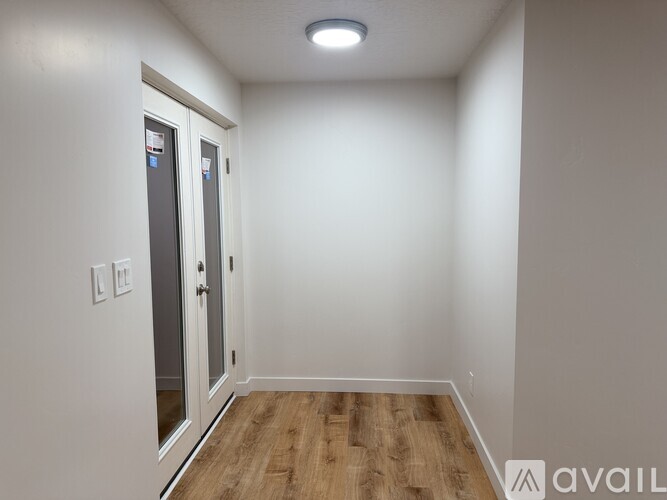 A room with a wooden floor and a white wall with a door and a light switch.
