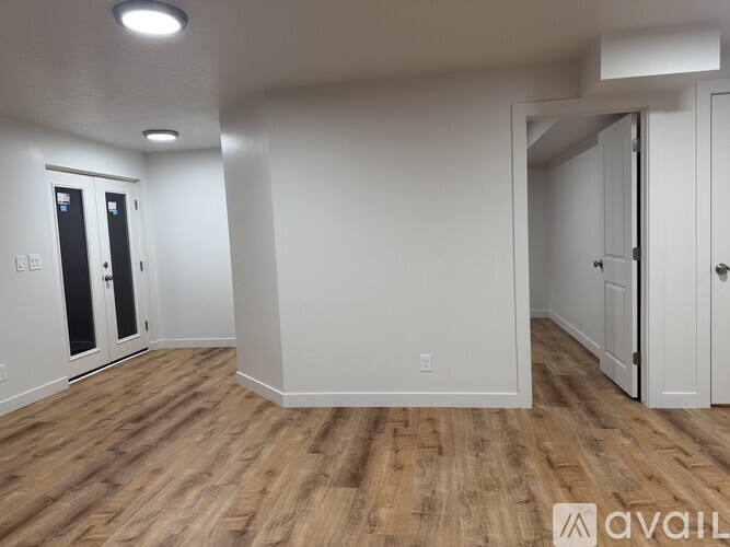A room with wood flooring and white walls, with two doors and a partially visible third door.