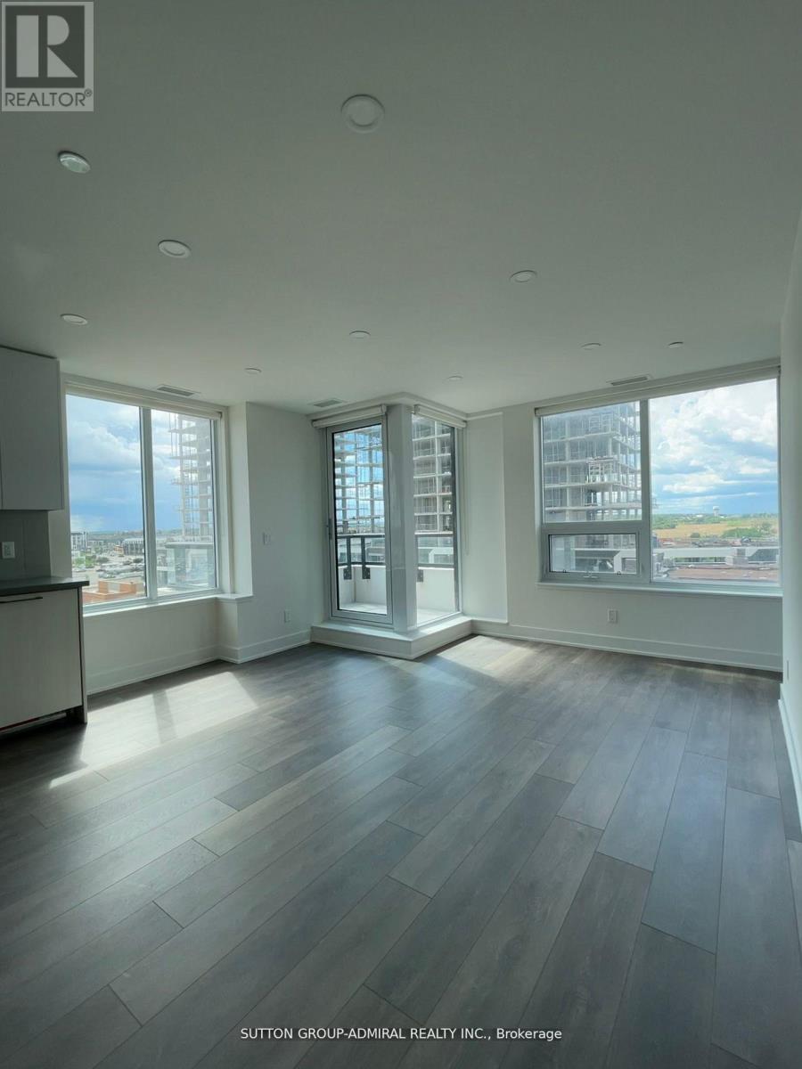 A spacious room with wood flooring and large windows overlooking the city.