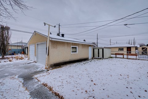A small building with a white door and a brown roof is surrounded by snow.