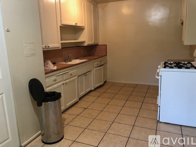 A kitchen with white cabinets and a black trash can.