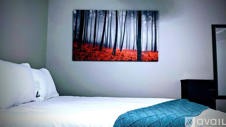 A bedroom with a bed, pillows, a painting on the wall, and a mirror.