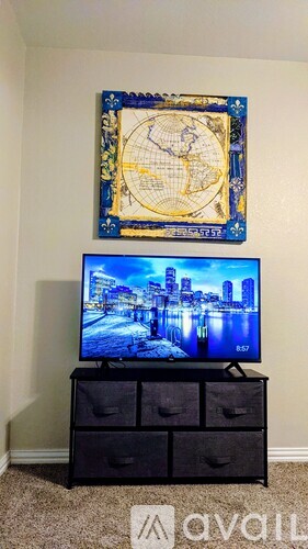 A flat screen TV is on a black stand with a framed globe on the wall behind it.