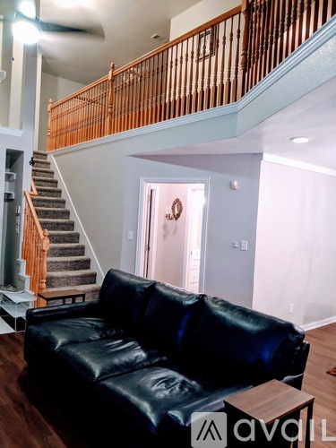 A black leather couch in a living room with a staircase in the background.