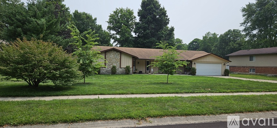 A house with a brown roof is surrounded by a green lawn and trees.