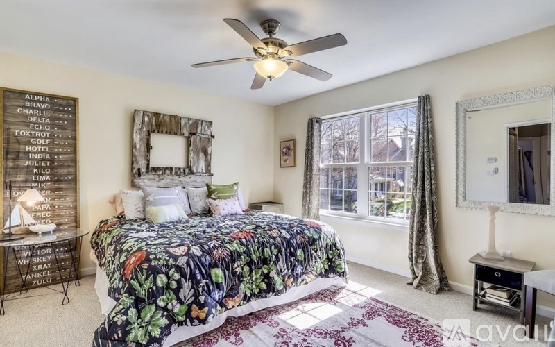A bedroom with a bed, a chest of drawers, a mirror, a window with curtains, and a chalkboard with names written on it.