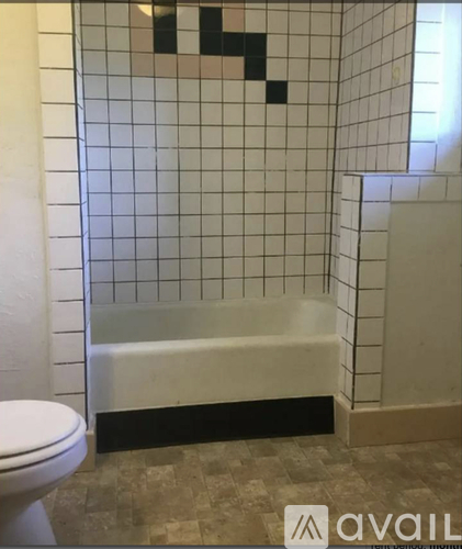 A bathroom with a white toilet and a white bathtub with black and white tiles on the wall.