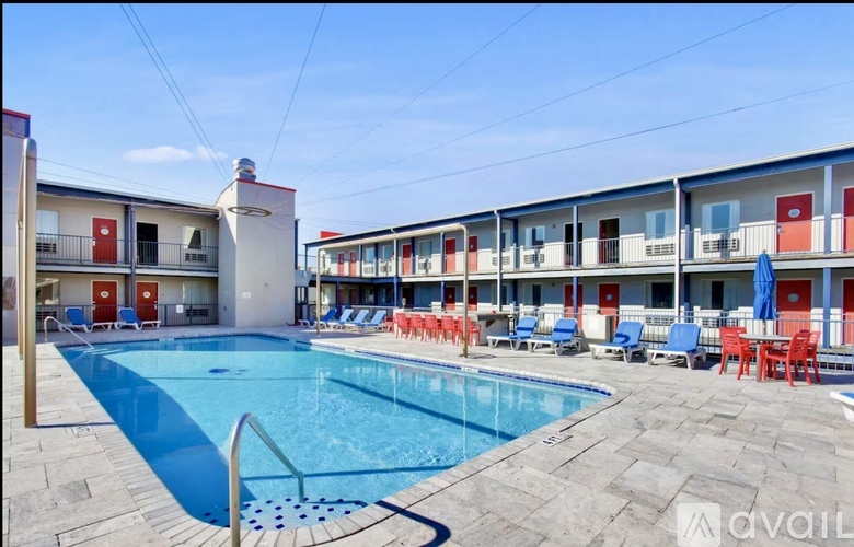 A pool area with chairs and umbrellas in front of a building with red doors.