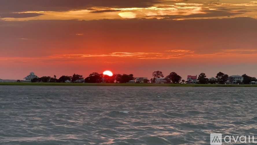 The sun is setting over a body of water with houses and trees in the background.