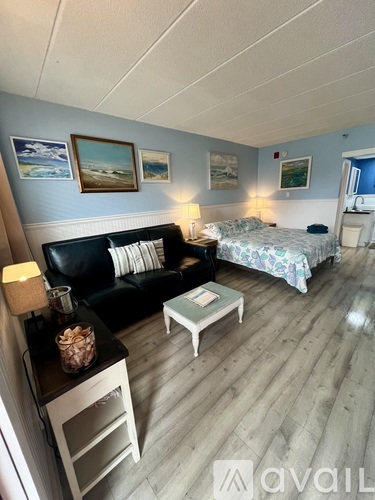 A living room with a black couch, a coffee table, and a bed with a white and blue comforter.