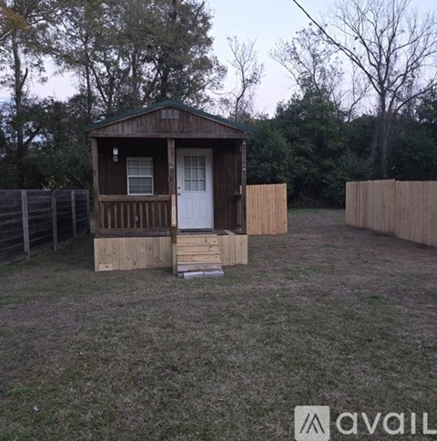 A small wooden cabin with a white door is situated in a grassy area.