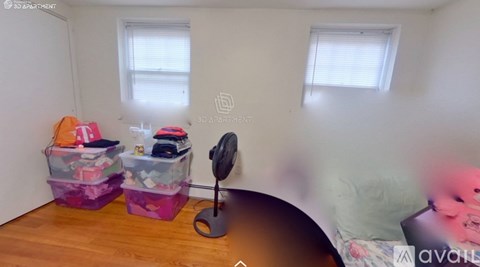 A room with a bed, a fan, and two plastic storage bins on the floor.