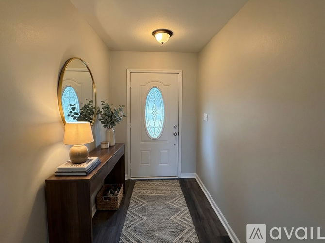 A hallway with a white door, a round mirror, a lamp, and a plant on a wooden table.