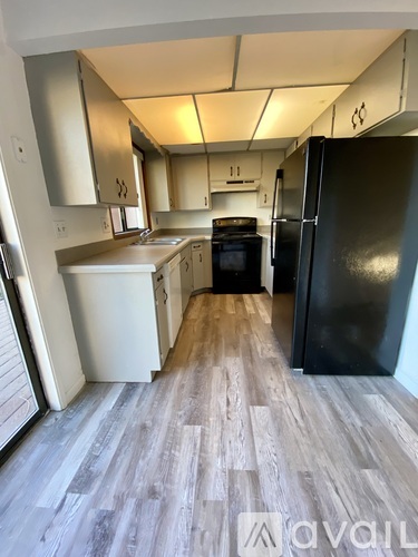 A kitchen with a black fridge and wooden floors.